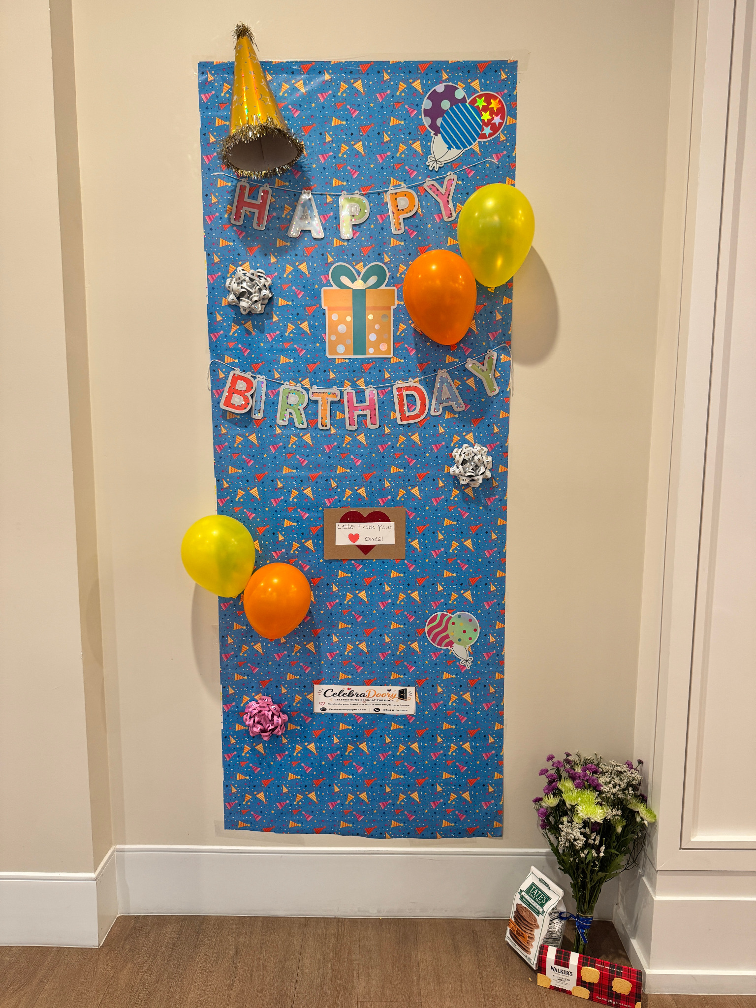 Blue Happy Birthday door decoration with balloons, bows, a party hat, flowers, treats, and a letter from loved ones