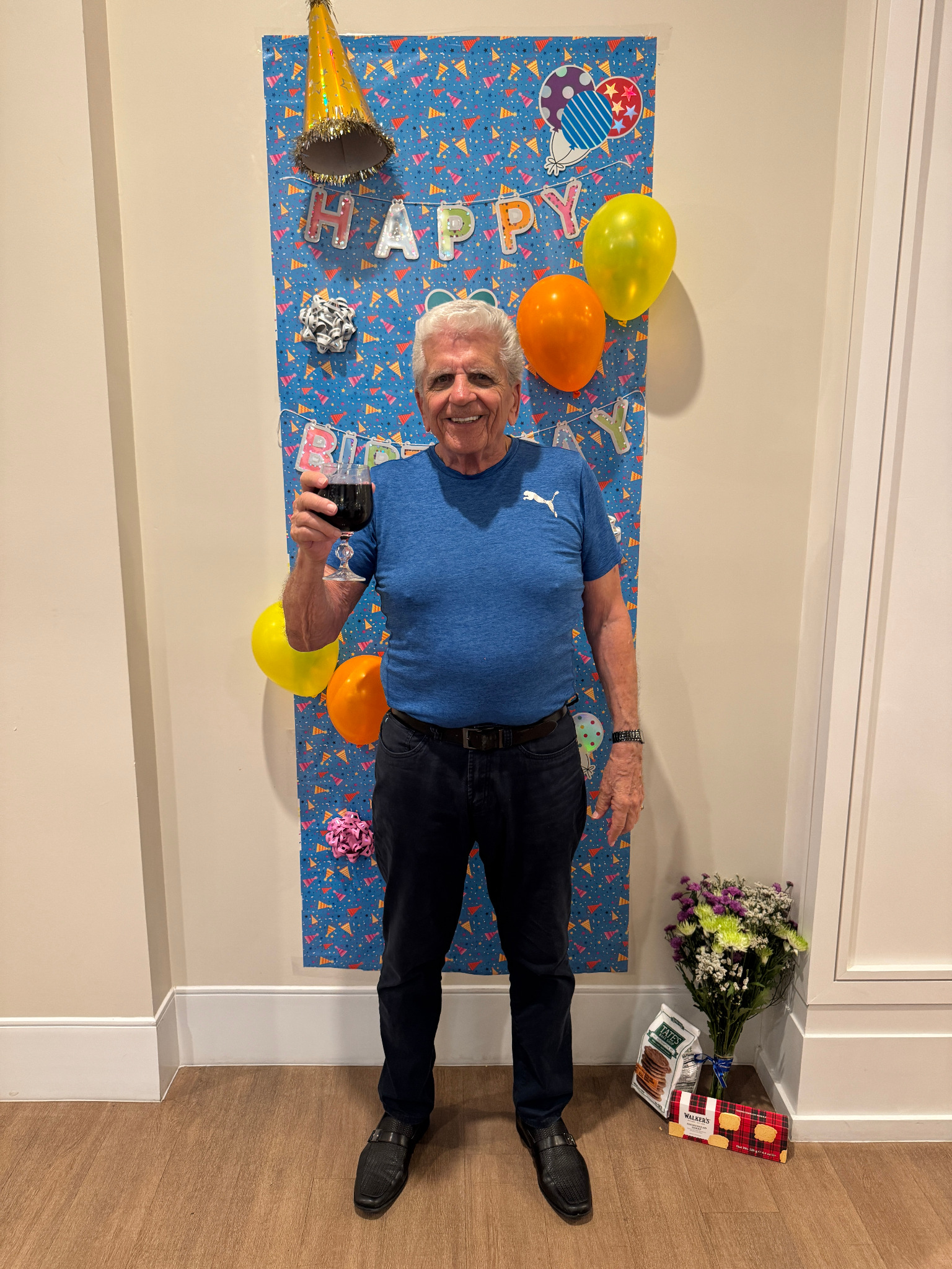 Smiling senior celebrating in front of a blue Happy Birthday door decoration with flowers and treats